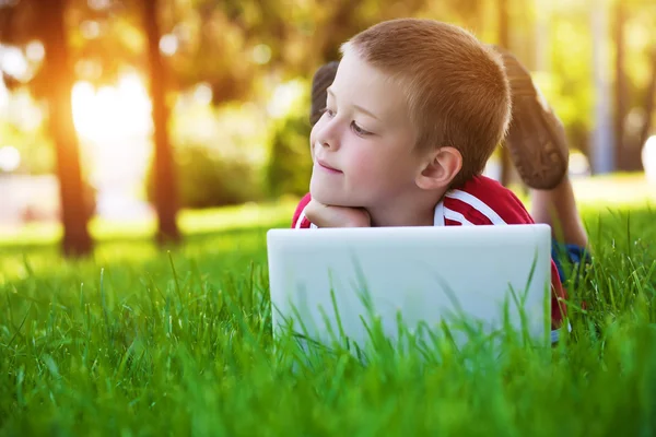 Šestiletý chlapec leží na zelené louce s notebookem — Stock fotografie
