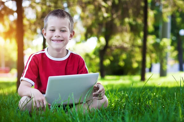 Pojken sitter med en laptop på gräset — Stockfoto