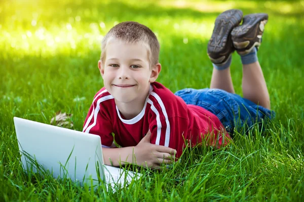 Six-year boy lying with a laptop on the grass — Stock Photo, Image