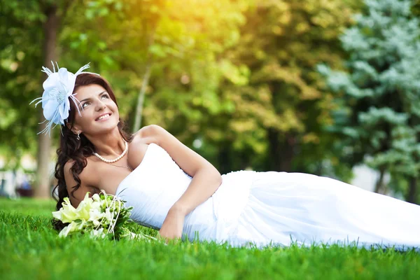 Happy bride in white dress lying on green grass — Stock Photo, Image