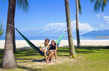 Attractive coulpe sitting in a hammock on a tropical beach clipart