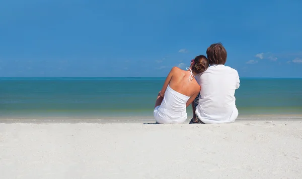 Νεαρό ζευγάρι συνεδρίαση για την παραλία με θέα στον ορίζοντα — Φωτογραφία Αρχείου