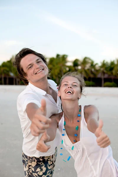 Šťastný pár, ukazující thumps up na pláži při západu slunce — Stock fotografie