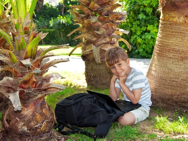 Boy with a netbook under a palm tree — Stock Photo, Image