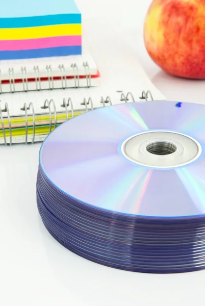Compact discs, color paper, copybook, apple on white desk — Stock Photo, Image