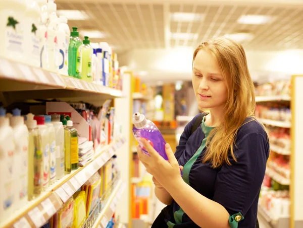 Mladá žena v supermarketu čtení nápis — Stock fotografie