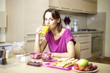 Portrait of female model drinking orange juice at home during breakfast clipart