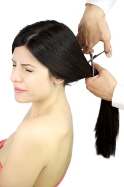 Beautiful woman keeping her eyes closed scared while hairdresser cuts her long ponytail clipart