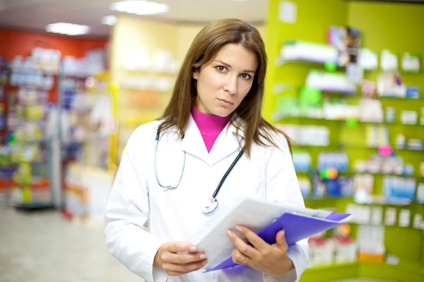 Серьёзная женщина-врач в аптеке с документами в руке — стоковое фото