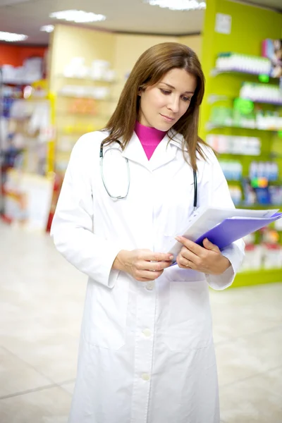 Poważne kobiece kobieta lekarz oglądanie dokumentów wewnątrz apteka — Zdjęcie stockowe