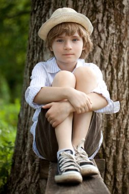 Boy in the hat on the bench clipart