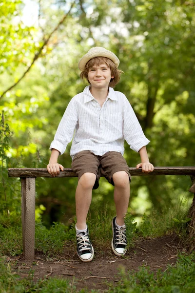 Menino de chapéu e calções sentado em um banco — Fotografia de Stock