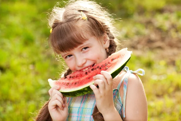 Engraçado, menina de cabelos escuros com tranças comendo uma melancia — Fotografia de Stock