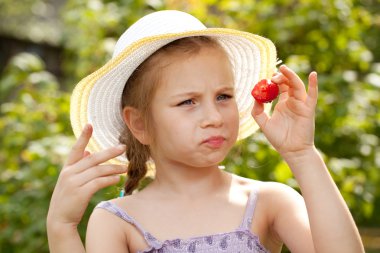 Girl in a summer hat considers strawberries clipart