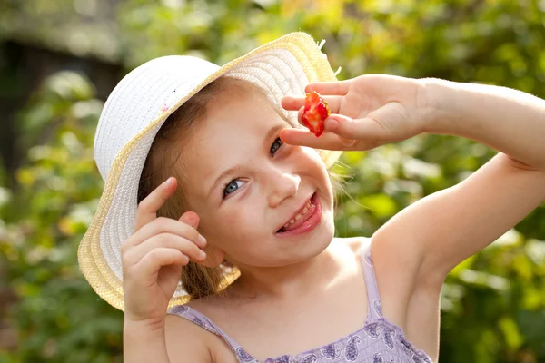 Mädchen mit Sommermütze und Kleid, das Erdbeeren isst — Stockfoto