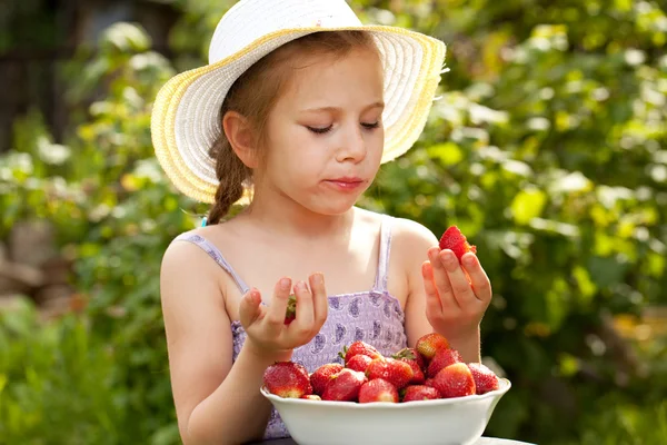 Girl in a summer hat and dress eating strawberries — Stock Photo, Image