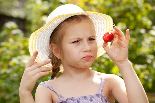 Girl in a summer hat considers strawberries — Stock Photo, Image
