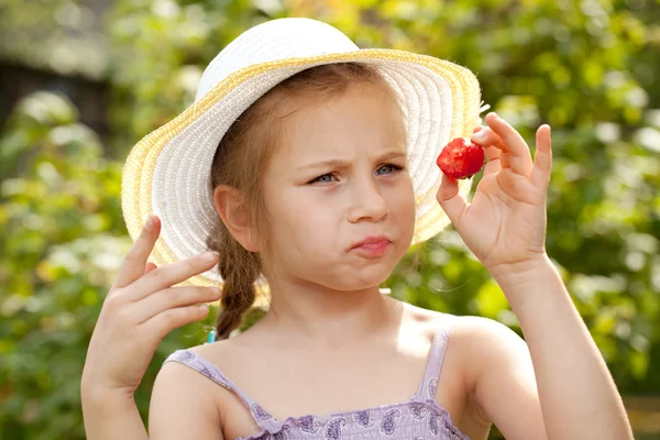 Mädchen mit Sommerhut betrachtet Erdbeeren — Stockfoto