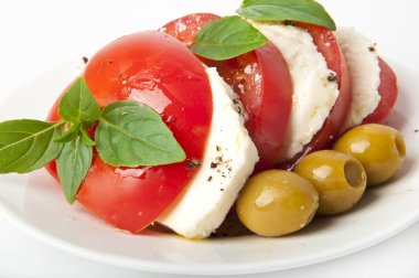 mozzarella ve domates dilimleri plaka ve beyaz bir arka plan üzerinde fesleğen yaprakları ile süslenmiş