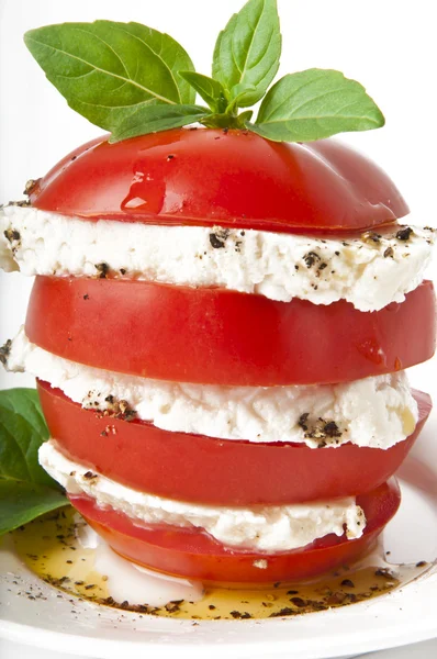 Rodajas de tomate y mozzarella decoradas con hojas de albahaca sobre un plato y fondo blanco — Foto de Stock