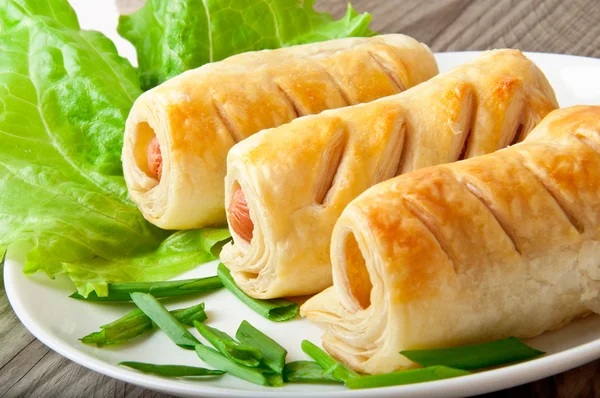 Sausage in the dough on a plate with greens — Stock Photo, Image
