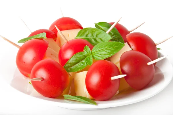 Tomaten- und Käsescheiben mit Basilikumblättern auf einem Teller und weißem Hintergrund dekoriert — Stockfoto