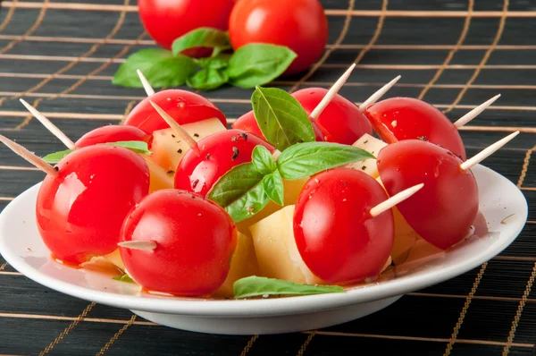 Tomato and cheese slices decorated with basil leaves on a plate — Stock Photo, Image