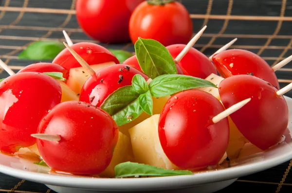 Bir tabakta fesleğen yaprakları ile süslenmiş domates ve peynir dilimleri — Stok fotoğraf