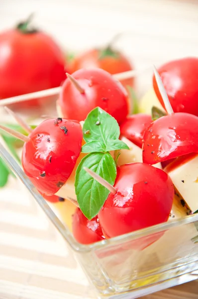 Ломтики томата и сыра, украшенные листьями базилика на тарелке и белом фоне — стоковое фото