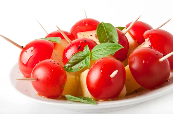 Rodajas de tomate y queso decoradas con hojas de albahaca sobre un plato y fondo blanco — Foto de Stock