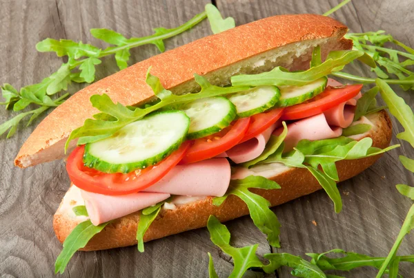 Smörgås med skinka, tomat, gurka, ruccola på gamla trä skärbräda — Stockfoto