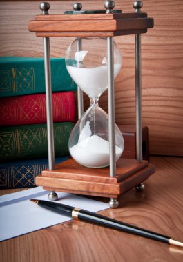 Hourglasses and book on a wooden table clipart