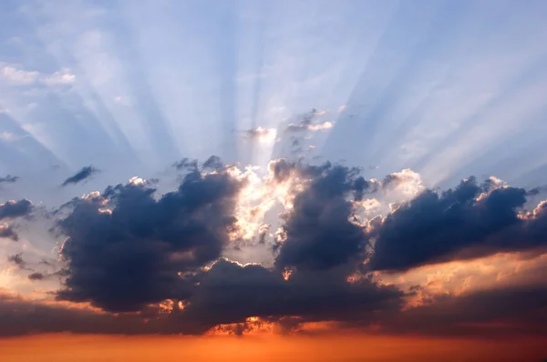 stock image The rays of the setting sun behind the clouds and blue sky.