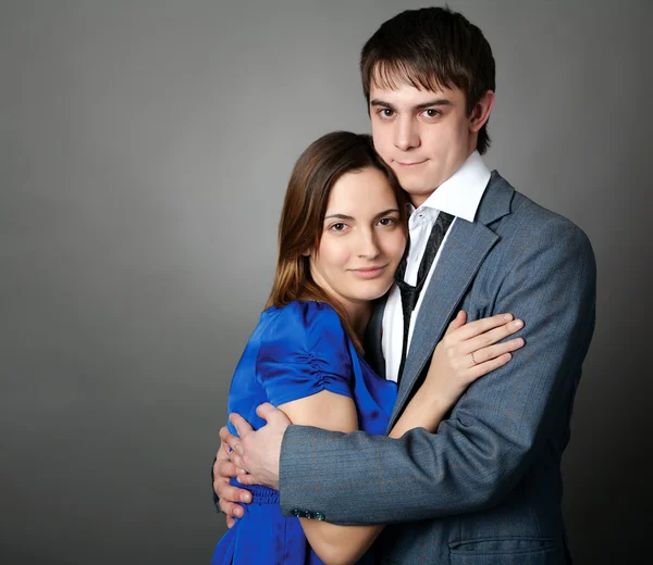 Young couple standing together against a grey wall — Stock Photo, Image