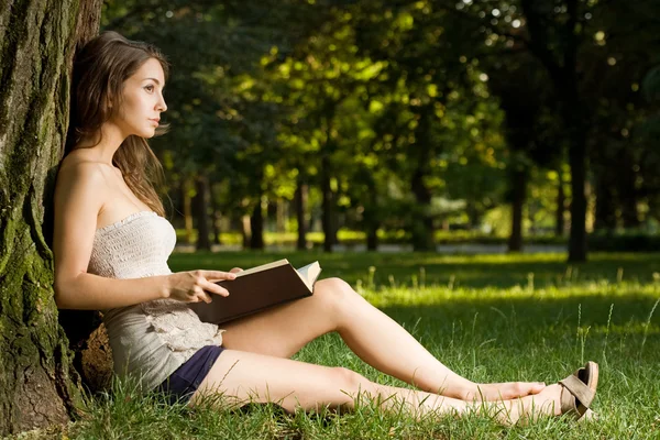 Hermosa morena leyendo un libro en el parque . — Foto de Stock
