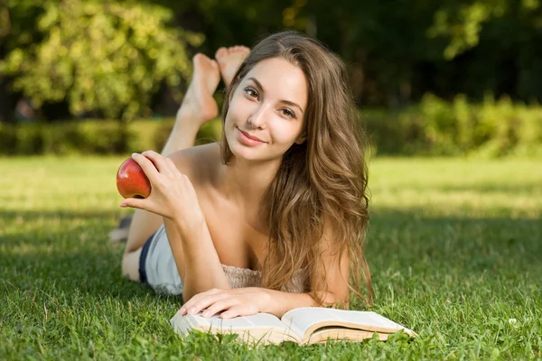 Cute young brunette in the park reading. — Stock Photo, Image
