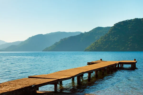 stock image Mountains and old wooden pier to the sea