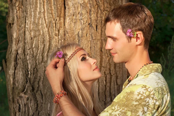 Young man decorates hair of beautiful blonde with flower — Stock Photo, Image