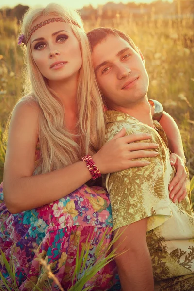 Cute young man and fine woman sit on meadow against sunset. — Stock Photo, Image