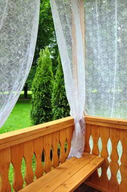 Wooden porch with lace curtains and garden view clipart