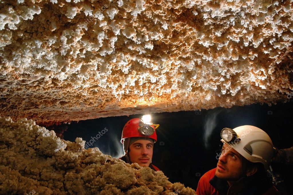 Beautiful stalactites in a cave with two speleologist explorers