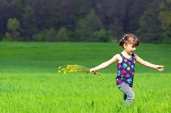 Niño con flores divirtiéndose al aire libre en el campo verde —  Fotos de Stock