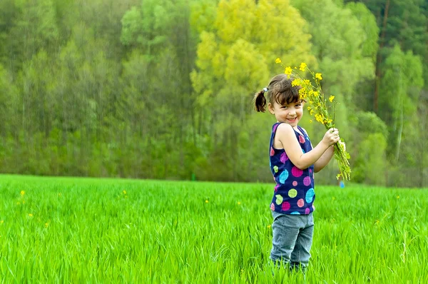Ragazzo con fiori divertirsi all'aperto sul campo verde — Foto Stock