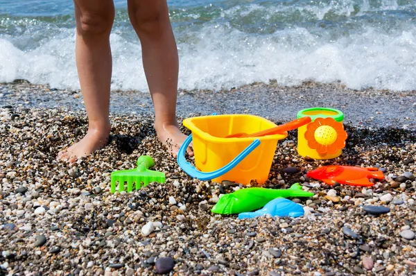 Pernas de criança e brinquedos na praia — Fotografia de Stock