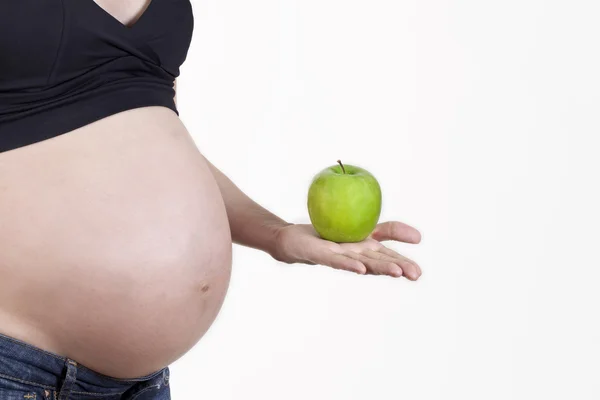 Pregnant woman's belly with and hand handing of green apple on white background — Stock Photo, Image