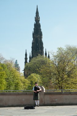 Scottish Piper playing with Edinburgh city background in May 2012 clipart
