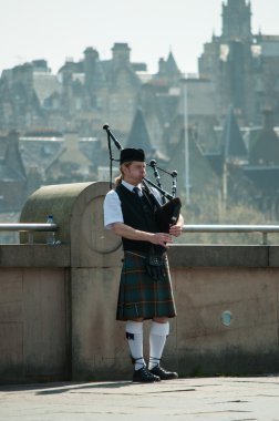 Scottish Piper playing with Edinburgh city background in May 2012 clipart