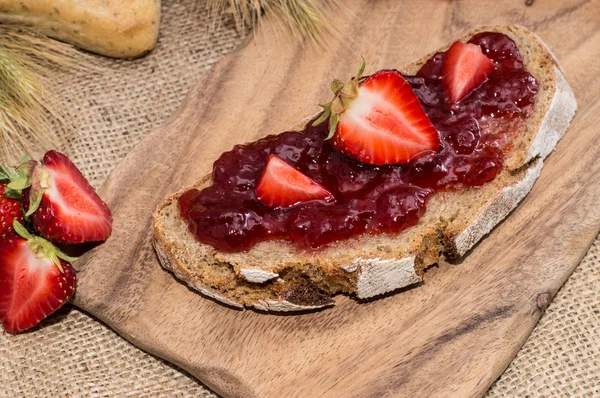 Brot mit Erdbeermarmelade auf Schneidebrett — Stockfoto