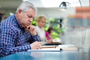 Senior man studying among young in library clipart