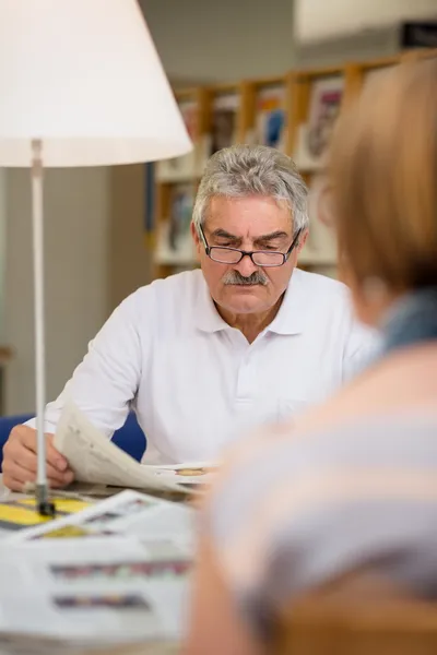 Senior man die krant leest met vrouw in bibliotheek — Stockfoto